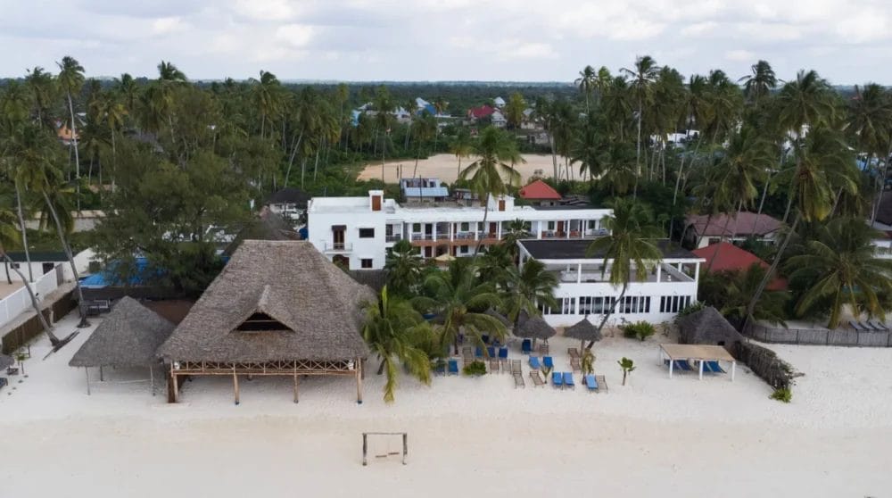 La vista aerea del BLU MARLIN BEACH RESORT mostra strutture con tetti di paglia, sabbia bianca, palme, lettini ed edifici bianchi immersi nella vegetazione tropicale. L'oceano è appena fuori dall'inquadratura di questa splendida destinazione di Marlin Beach.