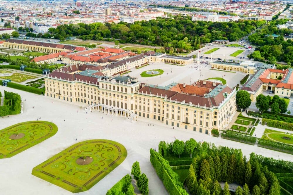 Una veduta aerea del Castello di Schönbrunn a Vienna, in Austria, mette in evidenza la sua architettura barocca gialla e i suoi giardini curati - una tappa iconica del Tour dell'Austria, con i sentieri alberati e il paesaggio urbano sullo sfondo.