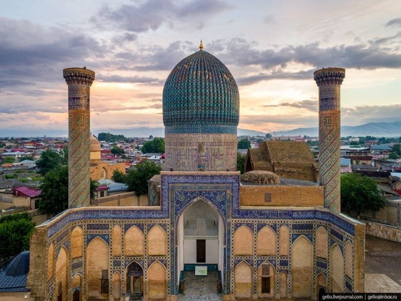 Veduta aerea del mausoleo Gur-e-Amir a Samarcanda, in Uzbekistan, che mostra la sua cupola di piastrelle blu, i due minareti ornati e gli intricati mosaici al tramonto: una tappa obbligata di ogni avventura di caravan tour in Uzbekistan.
