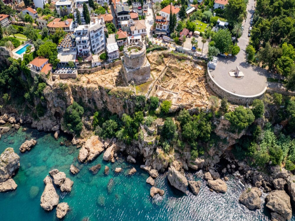Vista aerea di un'antica torre in pietra e di rovine su una scogliera che si affaccia sulle acque turchesi del mare di Bodrum, perfetta per un soggiorno mare Bodrum, circondata da case, alberi e coste rocciose in questa Istanbulissima città costiera.