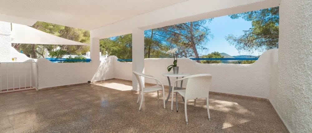 Ampia terrazza coperta del Globales Montemar con pareti bianche, un tavolino rotondo e due sedie bianche; le arcate aperte offrono una vista sugli alberi e sul cielo blu sullo sfondo.