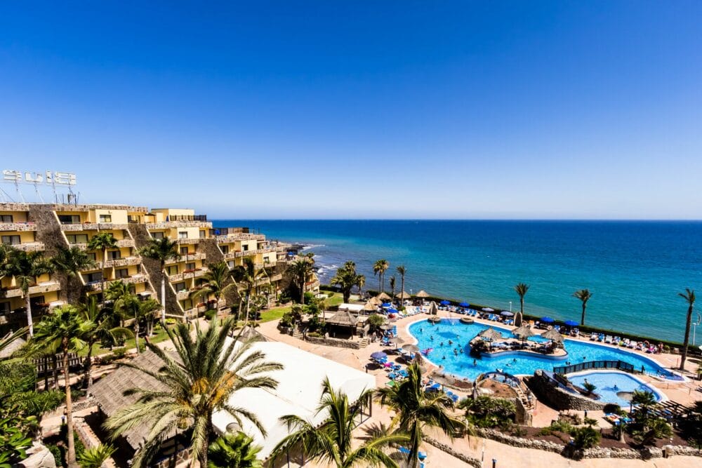 L'HOTEL BLUEBAY, un hotel a 4 stelle, è un resort sul mare con palme, una grande piscina all'aperto, lettini e edifici beige che si affacciano sull'oceano blu sotto un cielo limpido. Godetevi l'accesso esclusivo al BEACH CLUB per il massimo relax.