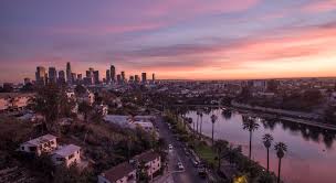 Una vista panoramica di Los Angeles al tramonto, con lo skyline della città, le palme e le case lungo uno specchio d'acqua calmo che riflette sfumature rosa e viola: un momento indimenticabile di ogni tour TOUR FOREVER WEST o Stati Uniti.