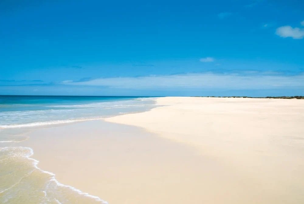 La spiaggia incontaminata e vuota del SEARESORT BOAVISTA è caratterizzata da una soffice sabbia bianca che si estende accanto a onde calme e turchesi sotto un cielo blu brillante: un paradiso invitante vicino al RIU KARAMBOA.